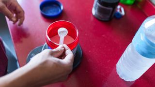 Hand holding scoop of white powdered supplement