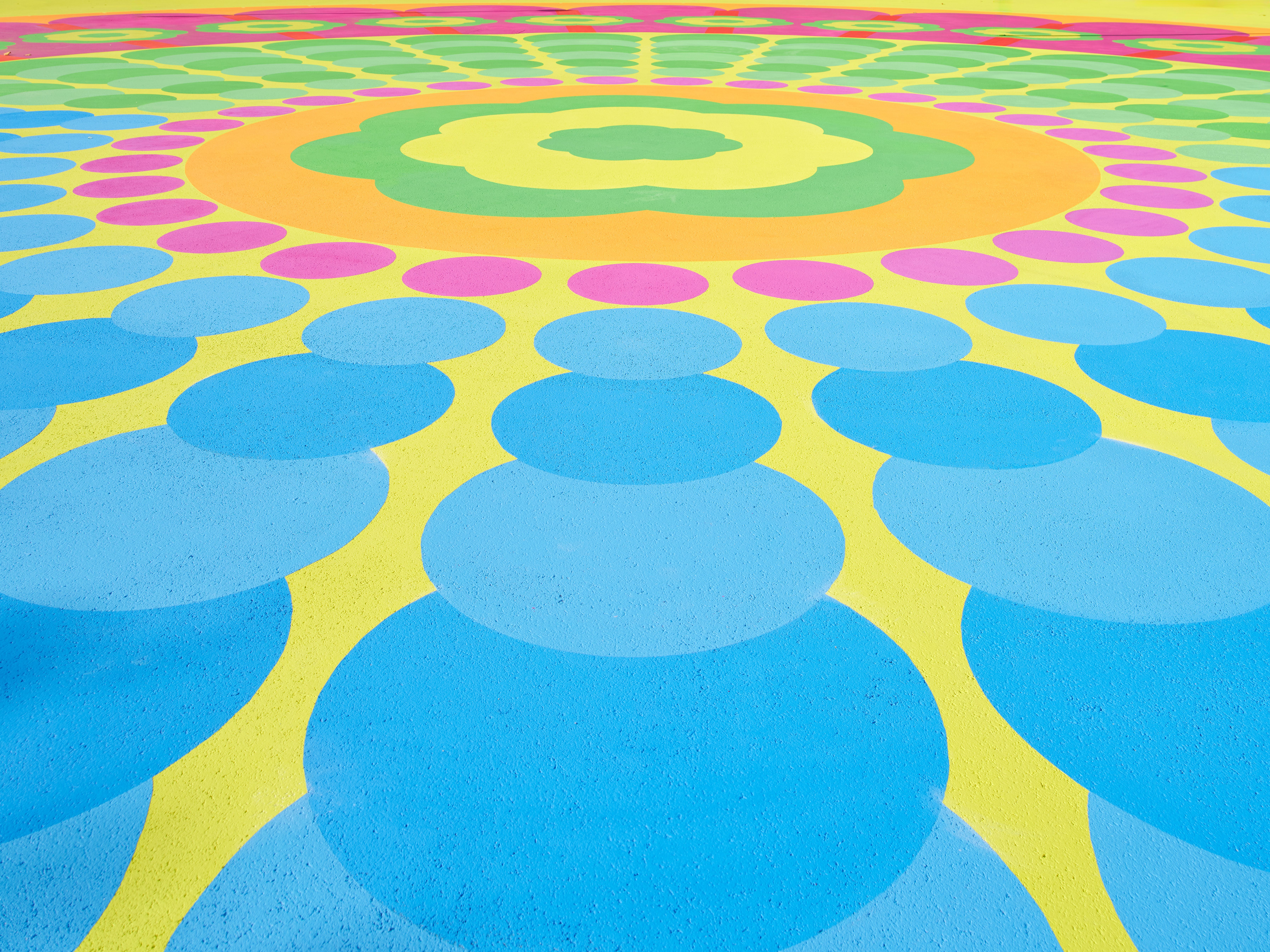 Aerial view of a colorful mural in pink, green, yellow, blue, and red tones, with organic shapes resembling flower petals.