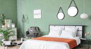 Green painted bedroom with mirrors placed above the bed