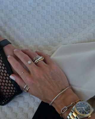 Woman wears several gold rings, watch, and diamond tennis bracelet.