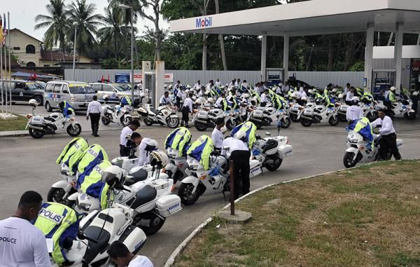 Police officers fill their motorcycles' gas tanks.