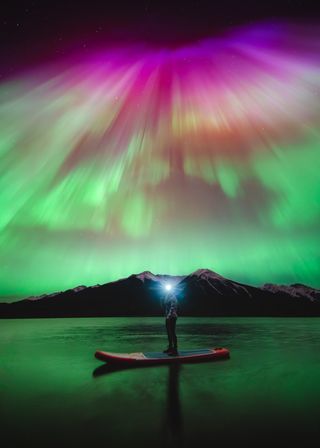 A photograph of the northern lights over a stand up paddleboarder