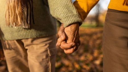 Hand close-up of mature couple holding hands while walking together on autumn day.