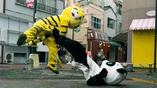 A teenager in a yellow tiger costume fights another teenager in a panda costume on a Japan city street, in 'Baby Assassins 2.'