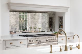 A small kitchen with antique burnished mirror backsplash,luxe gold accents, an island with sink and large cooker