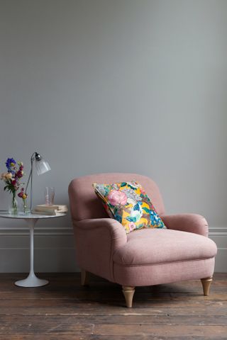 pink chair in room with wooden floor, grey walls and a side table with glowers, books and lamp