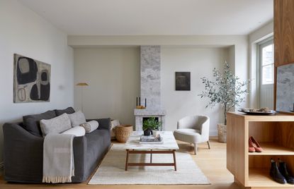 Lounge area with grey couch, white chair, table, rug, wooden shelves and wall painting.