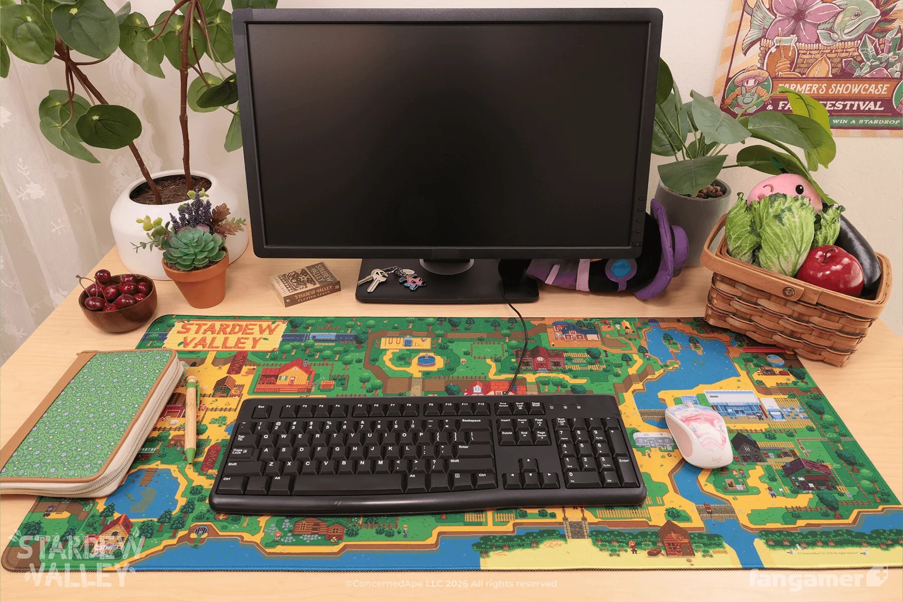 The Stardew Valley Pelican Town desk mat with a keyboard and monitor setup to show off how it looks in use.