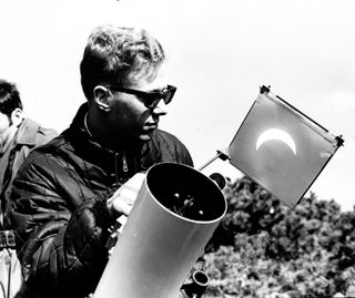 a man wearing a leather jacket and sunglasses looks at a projection of the sun during the solar eclipse.