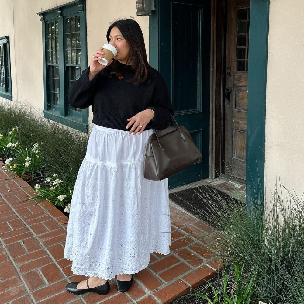Influencer @marina_torres wears a white skirt with black ballet flats and a black jumper.