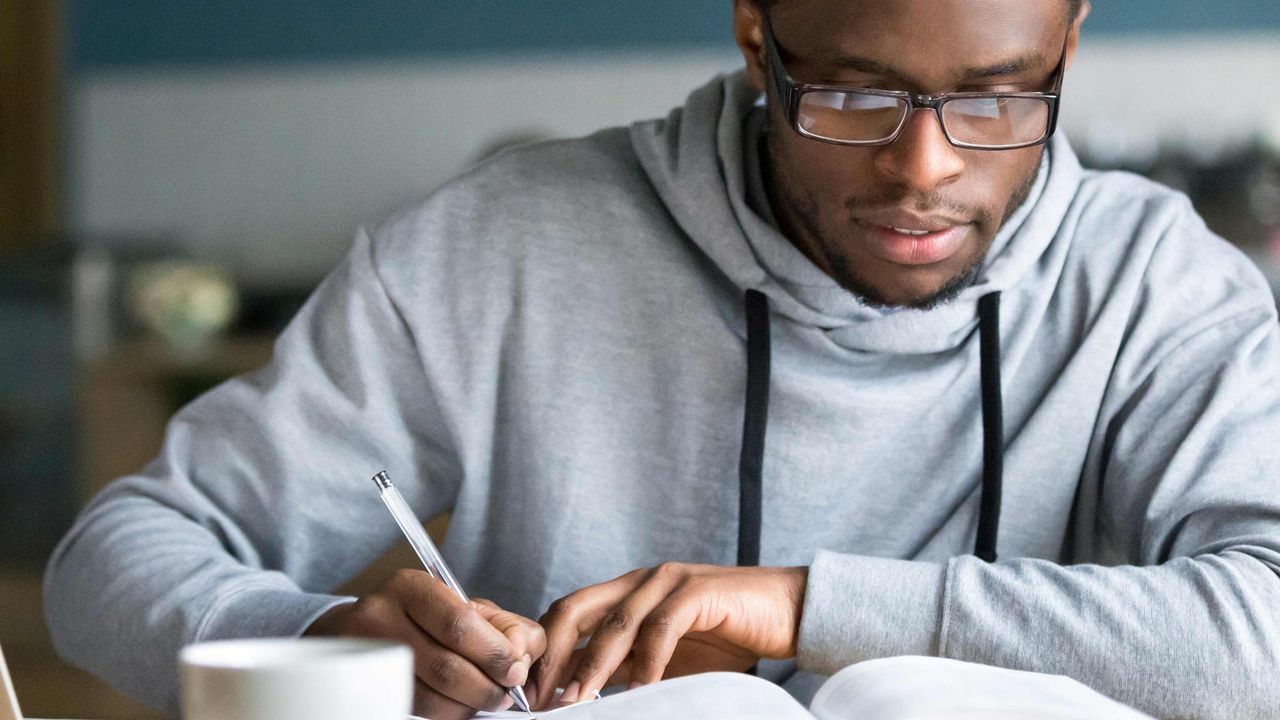 A young man takes notes as he studies a book.