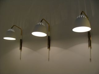 Three white pendant wall lights (all switched on) on a white wall