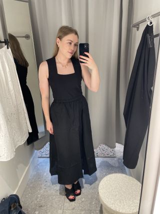 Woman in dressing room wears black tank top, black linen skirt and sandals