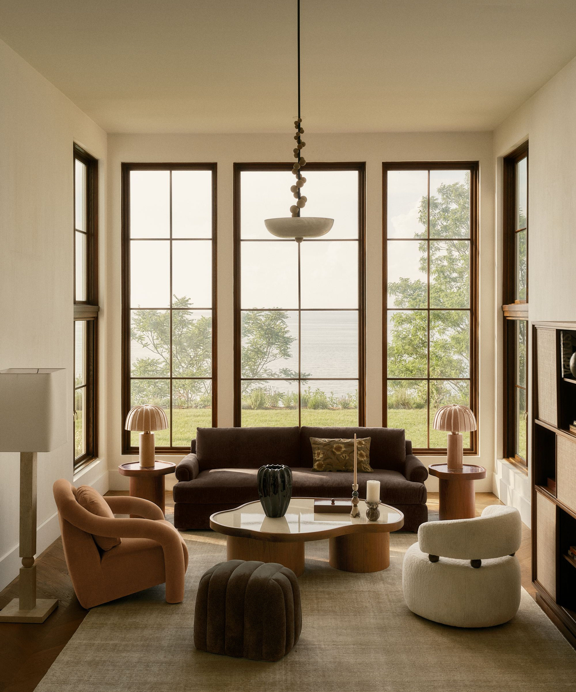 a living room with large windows, mis-matched furniture, a large coffee table, and a taupe area rug