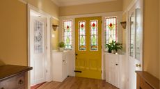 Hard wood floor, mustard front door and stained glass windows in entryway