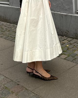 Woman wearing a white midi skirt and leopard print kitten heels.