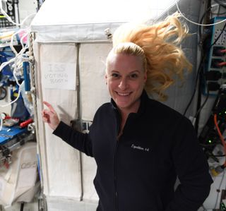 NASA astronaut Kate Rubins points to a sign on the International Space Station reading "ISS Voting Booth" in a photo she shared while announcing that she had voted from space.
