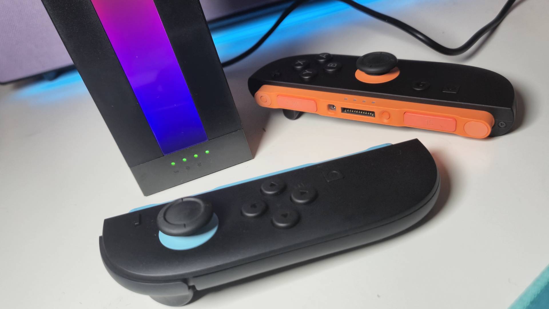Photo of the Switch 2 Joy-Con sitting on a white table with the Jsaux Energy Flow dock lit up between them.