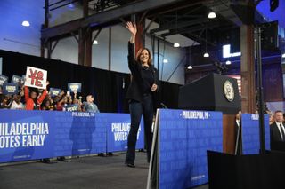 Kamala Harris waves onstage at a Philadelphia rally wearing a dark navy blazer with bootcut jeans and a pearl necklace