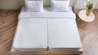 A split queen mattress on a bed frame with the bedding made neatly