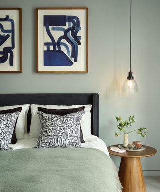 Modern bedroom with abstract art on wall, bed with fluffy throw, and wood round bedside table with foliage and hanging pendant light