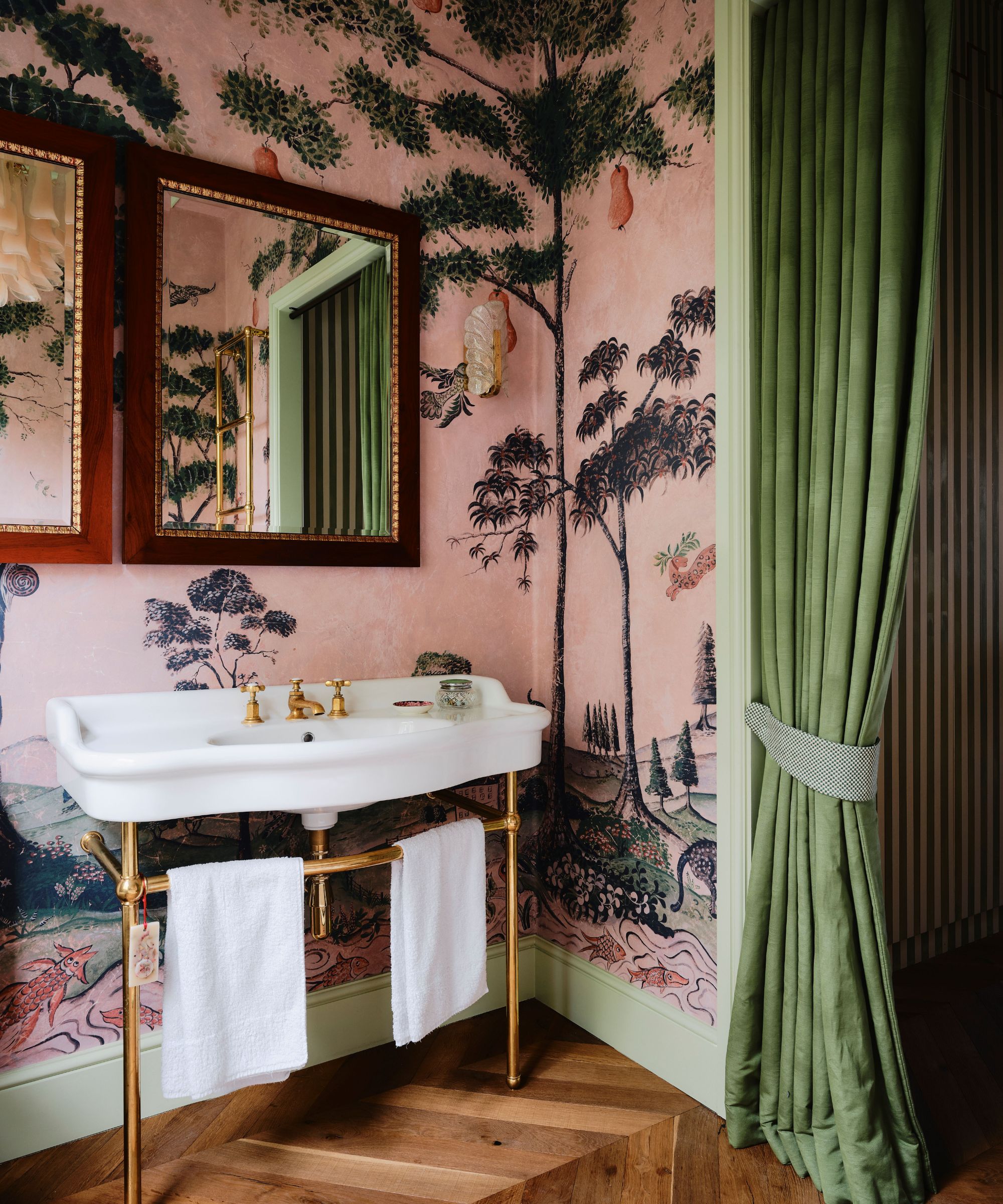 bathroom designed by studio duggan with a pink mural wallpaper, double wooden mirrors, traditional victorian vanity, and a green curtain