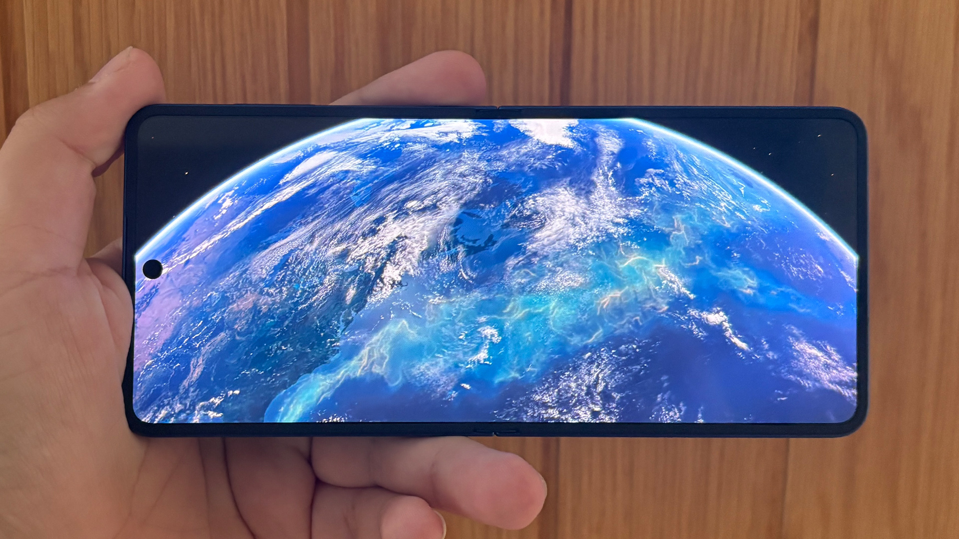 Samsung Galaxy Z Flip 7 smartphone held in hand in open position showing earth on screen