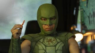 Judomaster holding a Flamin' Hot Cheeto while seated inside the back of a van in Peacemaker