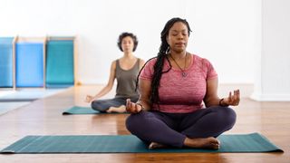 Woman with eyes closed, hands resting on legs crossed legs on yoga mat