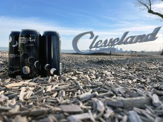 Three black cans with diagonal eclipse illustrations stand on woodchips near a sign that says Cleveland.