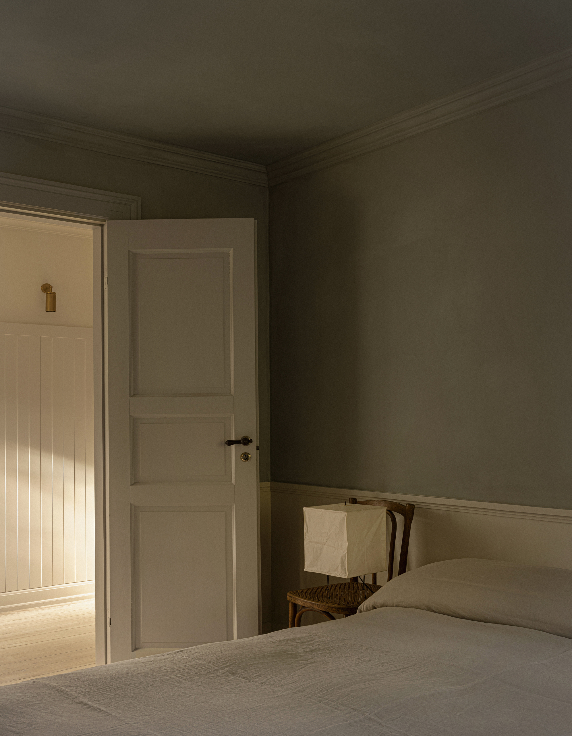 Image of a minimalist bedroom with a beige bed with no headboard in a room that is painted in a limewash olive and beige.