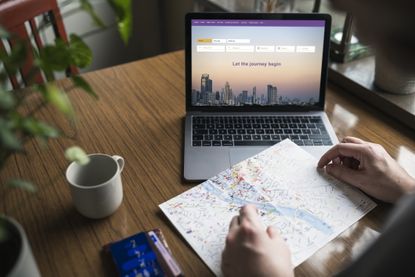 Man searching for flights on laptop and looking at map.