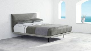 A Saatva Mattress placed on a foundation on a grey fabric base