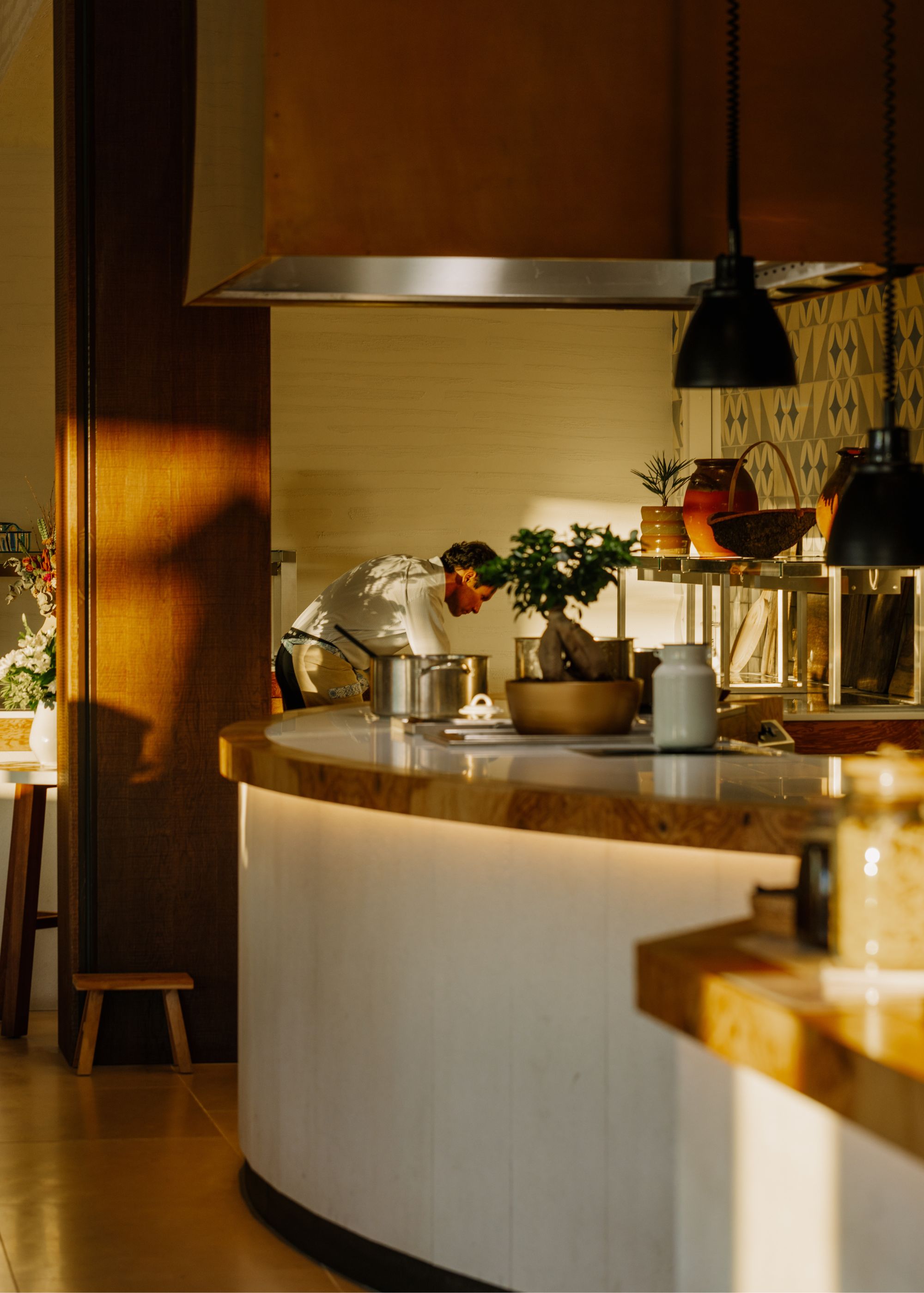 A kitchen with curved countertops and kitchen essentials such as a bowl, vase and lots more. There is also a staff member in the background. 