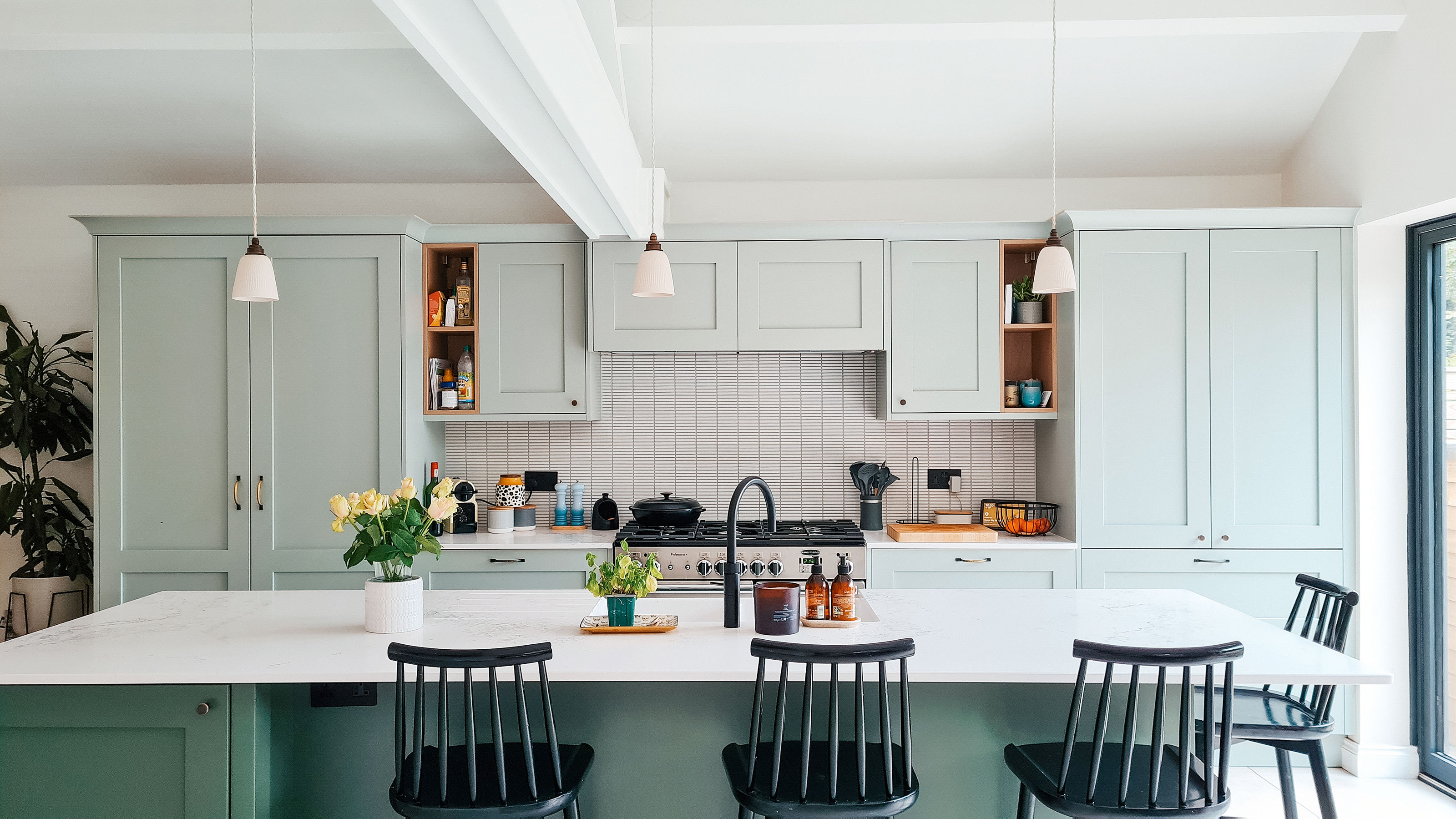 Green kitchen cabinets with black bar stools around kitchen island