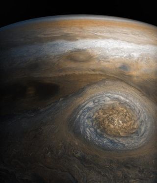 A white turbulent storm with orange in the middle brews on Jupiter