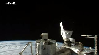 A white and black SpaceX Dragon Ax-2 capsule docked the space station with blue Earth behind.