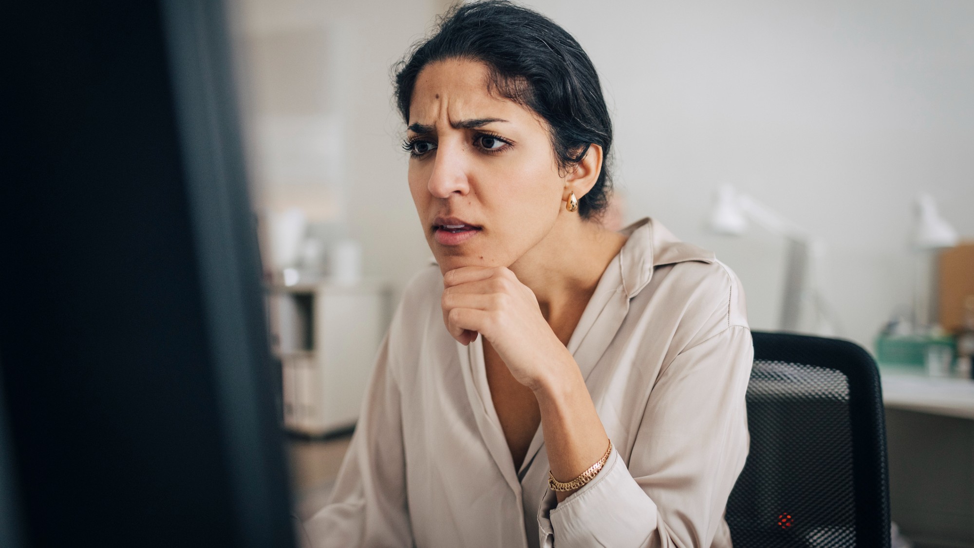 A confused woman looks at a computer screen.