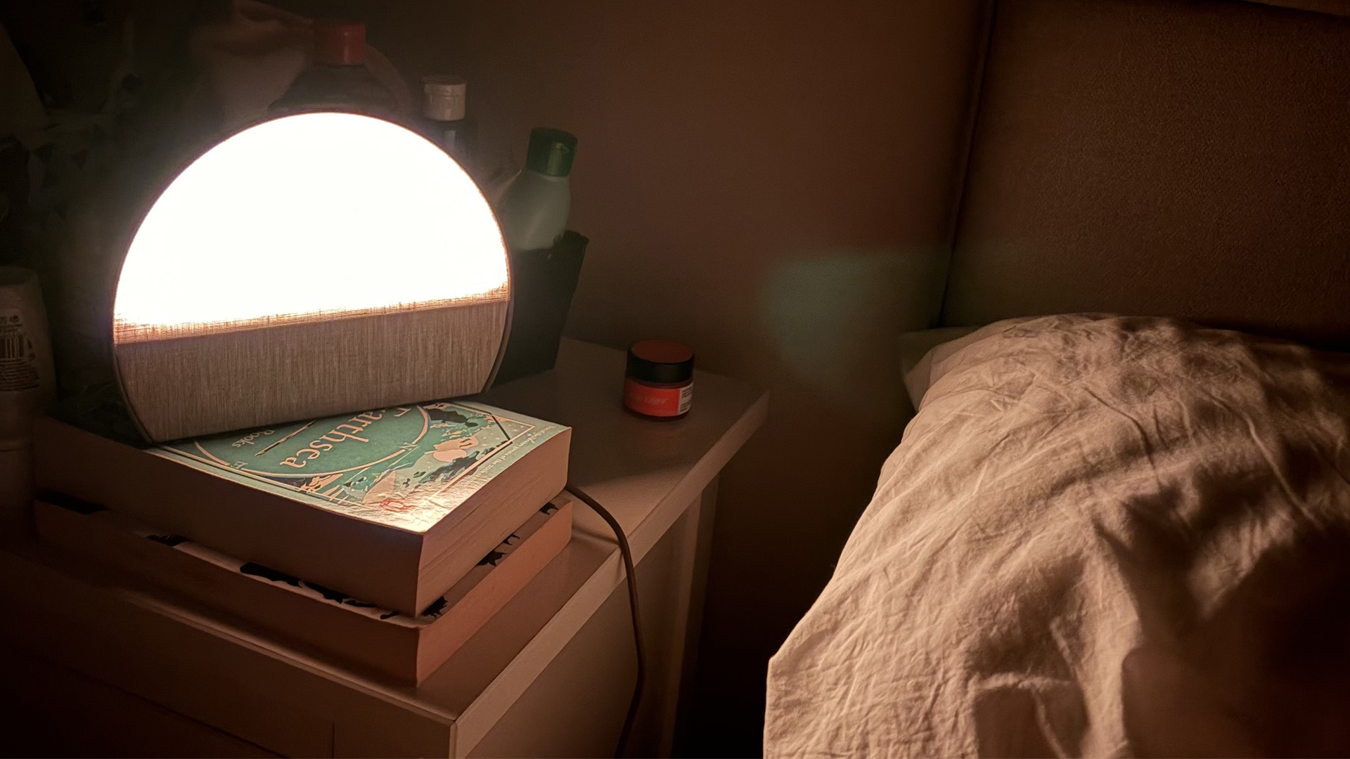 The Hatch Sleep Clock on a nightstand next to a bed, giving off a warm glow