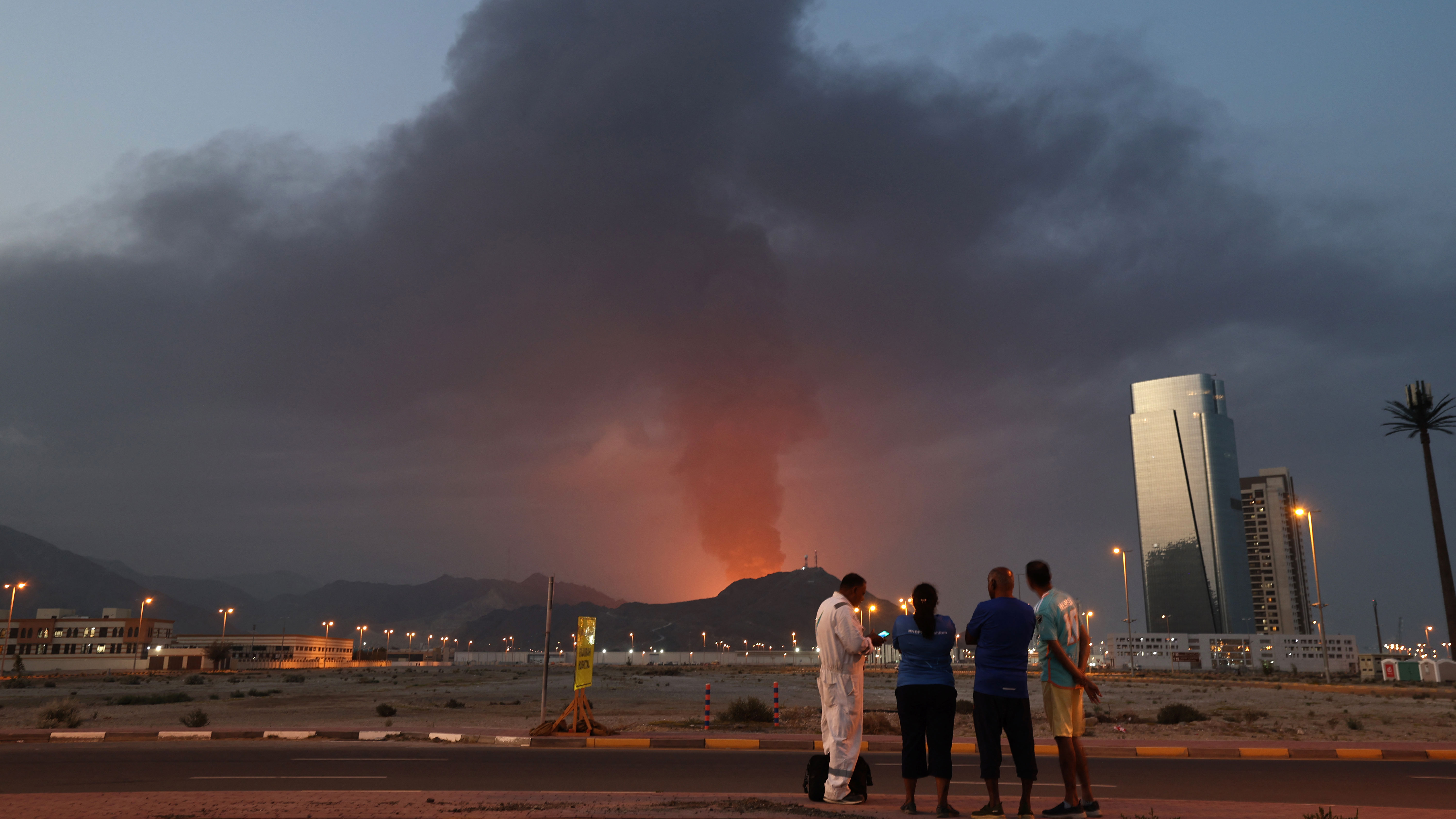 Explosion and fire in UAEForeign workers look at a tall plume of black smoke ascends following an explosion in the Fujairah industrial zone on March 3, 2026. Iran's strikes on Gulf neighbours since February 28, following the US-Israeli attack, forced the UAE to shut its airspace, blindsiding travellers who thought they were headed to one of the region's safest holiday destinations. (Photo by Fadel SENNA / AFP via Getty Images)