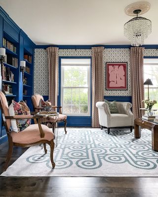 A traditional living room seating area with bold blue paint and a neutral white patterned wallpaper