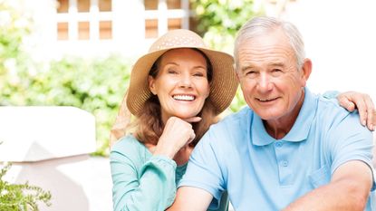 Portrait of happy senior woman with hand on chin sitting by man in garden. Horizontal shot.