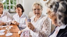 Senior female friends sitting around table playing cards