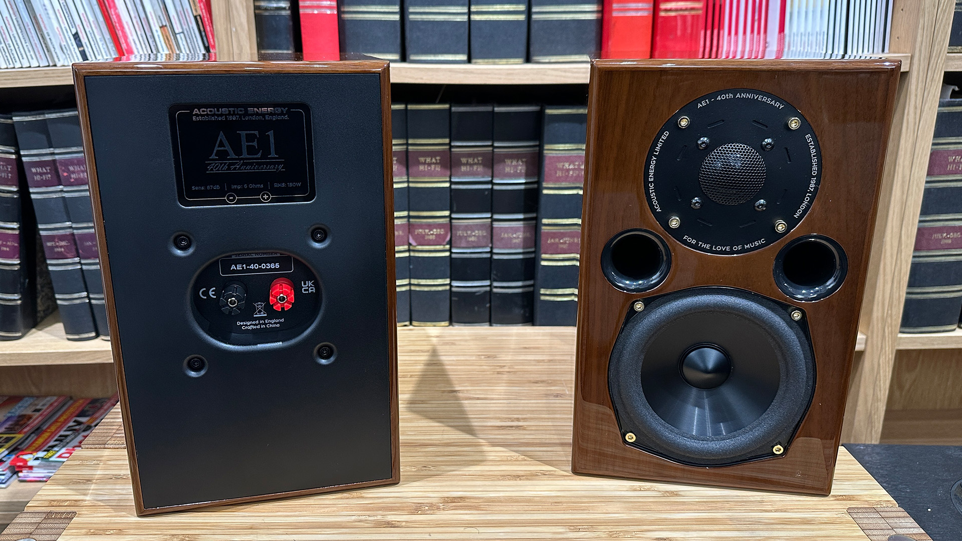 Acoustic Energy AE1 40th Anniversary standmount speakers on wooden hi-fi rack in front of bookcase