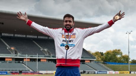 Martin Rooney wearing and holding gold medals in an athletics stadium