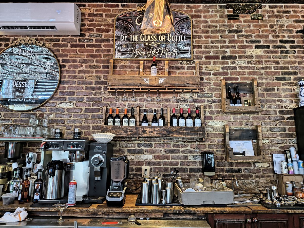 Rear counter of a bar showing bottles, a coffee machine and other drink-making equipment on a wooden table in front of an exposed brick wall