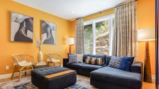 Small living room curtain ideas can transform a space, such as this yellow living room with curtains, a window, a blue couch and ottoman, and a colorful rug