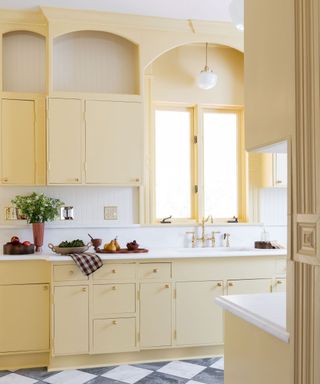 A kitchen drenched in butter yellow paired with white wall tiles and countertops and a black and white checkerboard floor