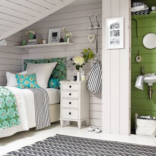 attic bedroom with painted floorboards and weatherboard and drawer units