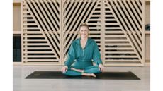 woman dressed in jade green sitting cross legged in a studio setting, facing the camera smiling